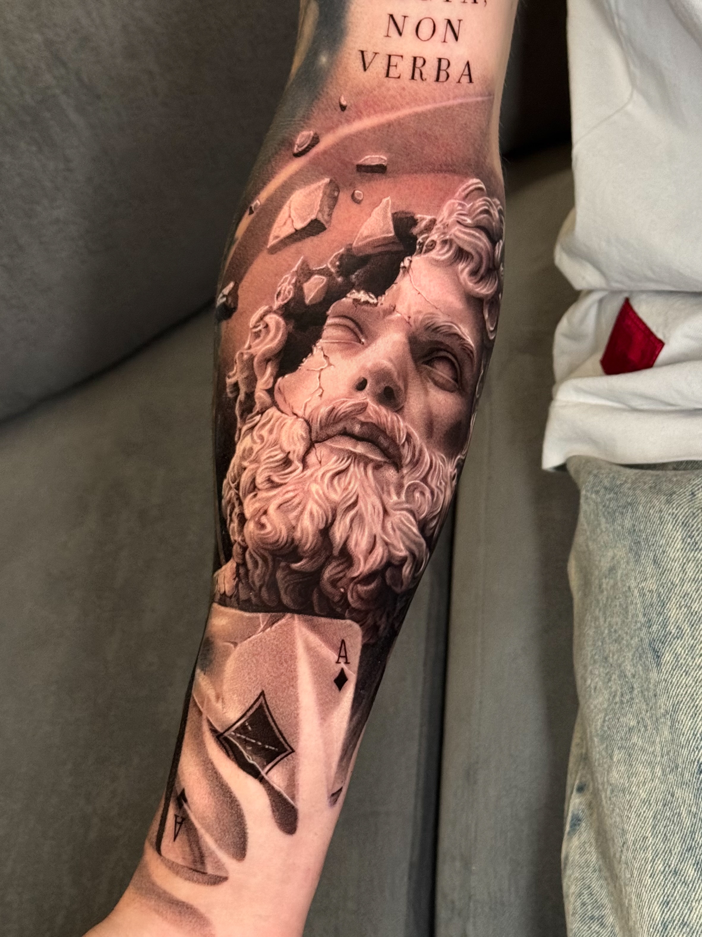 Estatua del Tiempo, rostro de escultura clásica agrietándose con cartas de póker, tatuaje de antebrazo en realismo de sombras